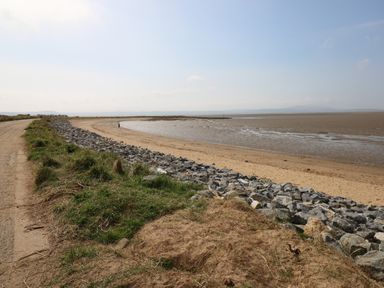 A coastal scene with a sandy beach a curved shoreline rocky embankment and a dirt path at 5 Pontardulais Road in Llangennech