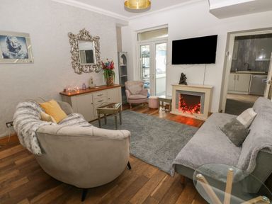 A living room with sofas, a coffee table, a wall mirror, a television above an electric fireplace and a doorway leading to a kitchen at 5 Pontardulais Road in Llangennech