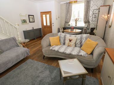 A living room with a curved sofa, yellow pillows, a small table, and a dining table by the window at 5 Pontardulais Road in Llangennech