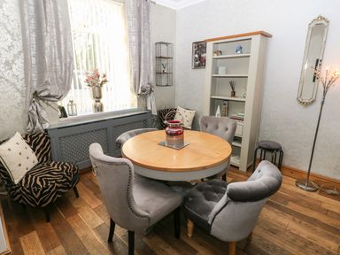 A dining room with round wooden table surrounded by grey chairs and a cabinet with shelves at 5 Pontardulais Road in Llangennech