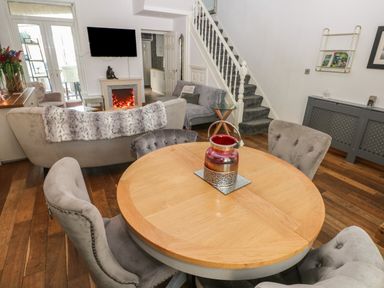 A dining area with a round wooden table and gray chairs next to a living room with sofas and a wall-mounted TV at 5 Pontardulais Road in Llangennech
