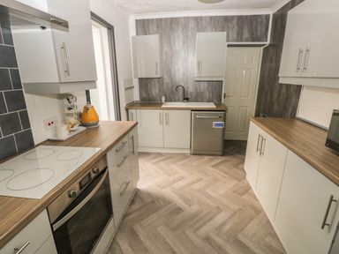 A kitchen with white cabinets wooden countertops a built in oven cooktop a dishwasher and a microwave at 5 Pontardulais Road in Llangennech