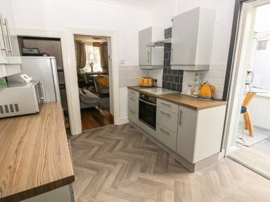 A kitchen with wooden countertops grey cabinets orange kettle and toaster opening to a dining area and another room at 5 Pontardulais Road in Llangennech