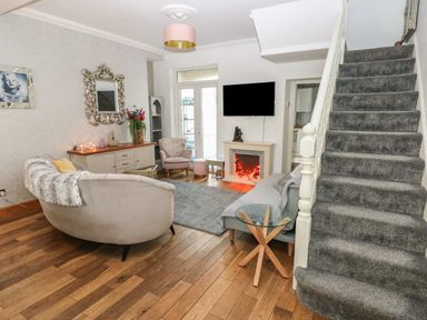 A living room with a curved sofa a gray armchair a gray carpet and stairs at 5 Pontardulais Road in Llangennech