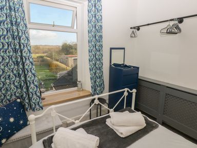 A bedroom with a white metal bed frame towels on the bed patterned curtains and a blue chest of drawers at 5 Pontardulais Road in Llangennech