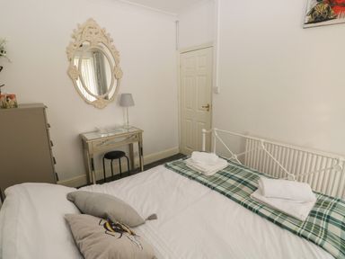 A bedroom with a bed with towels and pillows a mirror above a desk with a lamp and a stool at 5 Pontardulais Road in Llangennech