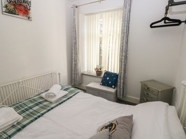 A bedroom with a bed with folded towels a window with vertical blinds and curtains a small chest of drawers and an ottoman at 5 Pontardulais Road in Llangennech