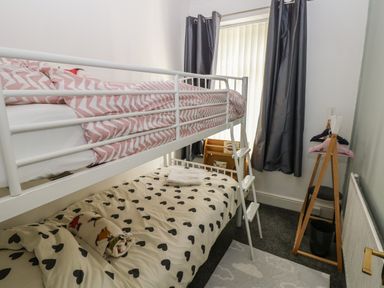 A small bedroom with a white metal bunk bed a wooden clothes rack with hangers and dark curtains at 5 Pontardulais Road in Llangennech
