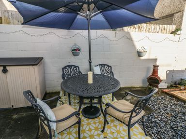 An outdoor patio with a round metal table and four chairs under a blue umbrella with a candle on the table at 5 Pontardulais Road in Llangennech