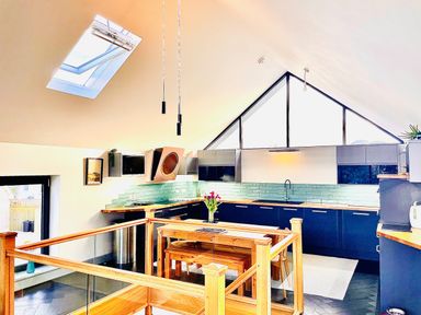 A kitchen with blue cabinets wooden countertops and a wooden dining table with flowers at Avalennek in St Newlyn East