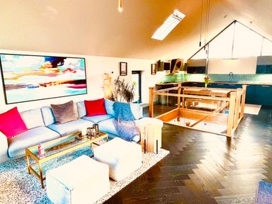 A living room with a sectional sofa and coffee table next to a kitchen area with a dining table at Avalennek in St Newlyn East