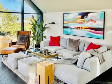 A living room with a gray sofa red and gray pillows a brown armchair glass coffee table and large windows at Avalennek in St Newlyn East