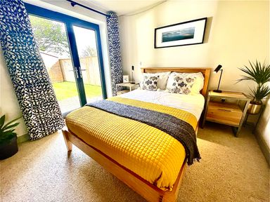 A bedroom with a wooden bed yellow bedding and glass doors leading outside at Avalennek in St Newlyn East