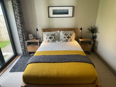 A bedroom with a bed with yellow and gray blankets and two bedside tables with lamps at Avalennek in St Newlyn East