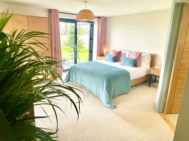 A bedroom with a bed a plant bedside tables and glass doors leading to a garden at Avalennek in St Newlyn East
