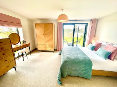 A bedroom with a bed pillows wardrobe dresser vanity table and chairs outside the glass doors at Avalennek in St Newlyn East