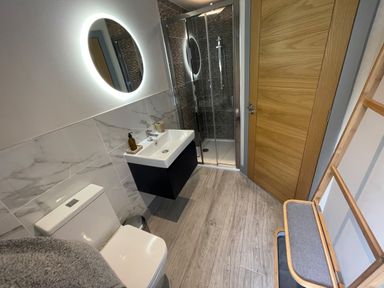 A bathroom with a toilet sink mirror shower and wooden door at Avalennek in St Newlyn East