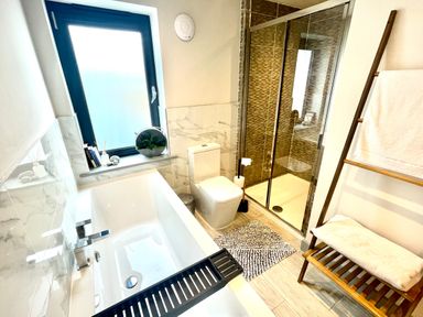 A bathroom with a bathtub toilet shower wooden towel rack and a window at Avalennek in St Newlyn East