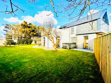 A backyard with a lawn trees a wooden fence and a modern house at Avalennek in St Newlyn East