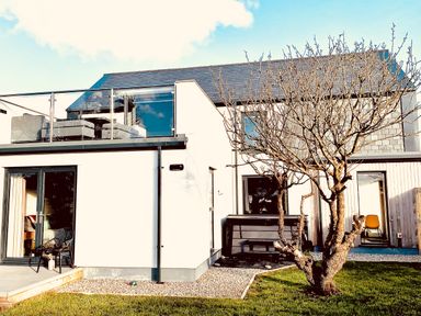 A modern two-story house with a balcony and glass railing a tree in front and a grassy yard at Avalennek in St Newlyn East