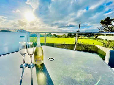 A balcony with a table holding a bottle and two glasses overlooking a green field at Avalennek in St Newlyn East