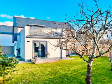 A modern two-story house with a balcony and patio chairs in a garden with leafless trees at Avalennek in St Newlyn East