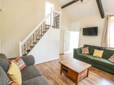 A living room with two sofas a wooden coffee table a wall mounted tv a staircase with wrought iron railing at Y Bwthyn Bach in Tregarth
