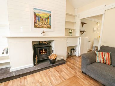 A living room with a wood-burning stove fireplace a gray sofa with a colorful cushion and a painting above the fireplace at Y Bwthyn Bach in Tregarth