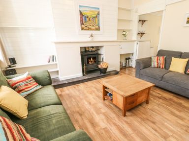 A living room with two sofas a wooden coffee table and a fireplace with fire burning at Y Bwthyn Bach in Tregarth