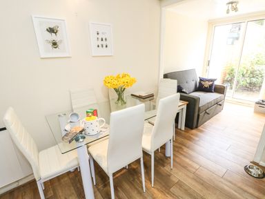 A dining area with a glass table and white chairs next to a sitting area with a gray loveseat and sliding glass doors at Y Bwthyn Bach in Tregarth