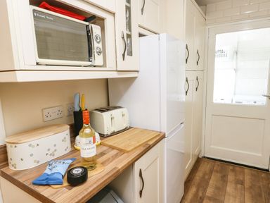 A kitchen counter with a microwave oven bread bin toaster bottle of wine and packets with cabinets and a door to a utility area at Y Bwthyn Bach in Tregarth