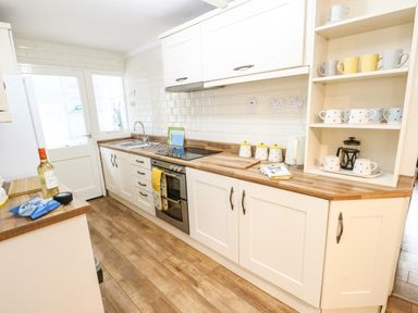 A kitchen with white cabinets wooden countertops and a door with window at Y Bwthyn Bach in Tregarth