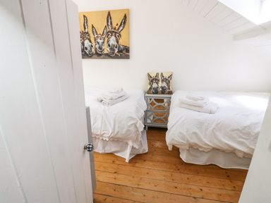 A bedroom with two single beds white bedding a bedside table and donkey artwork at Y Bwthyn Bach in Tregarth