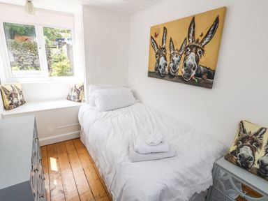 A small bedroom with a single bed a window with donkey cushions and a donkey painting on the wall at Y Bwthyn Bach in Tregarth
