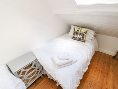 A small bedroom with a bed white linens a bedside table and wooden floor at Y Bwthyn Bach in Tregarth