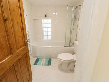 A bathroom with a wooden door a white bathtub with shower and a toilet at Y Bwthyn Bach in Tregarth