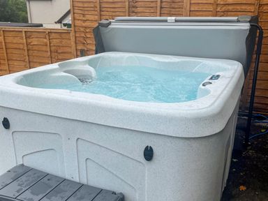 An outdoor hot tub filled with water next to a wooden fence with a gray hot tub cover at Y Bwthyn Bach in Tregarth