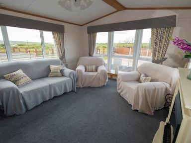A living room with sofas armchairs cushions curtains and large windows at The Lodge in Rhosybol