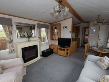 A living room with a fireplace a television a dining table and chairs at The Lodge in Rhosybol
