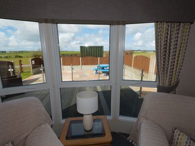 A sitting area with two sofas a small table with a lamp and large windows looking out to a patio and fields at The Lodge in Rhosybol