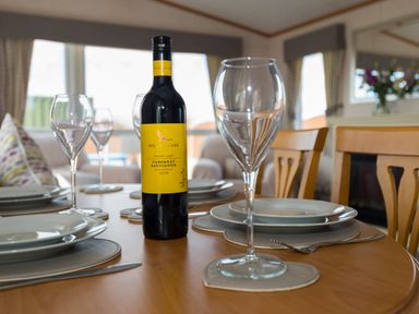 A dining table set with plates wine glasses and a bottle of wine at The Lodge in Rhosybol