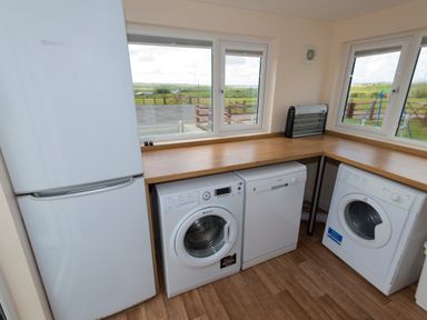 A utility room with a fridge freezer washing machine dishwasher and drying machine under a wooden countertop at The Lodge in Rhosybol