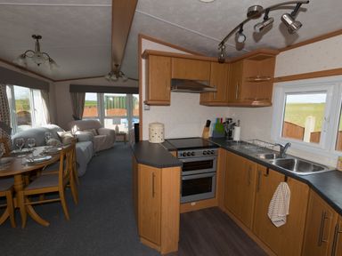 An open kitchen and dining area with wooden cabinets a double sink an oven and a dining table with chairs set for a meal at The Lodge in Rhosybol