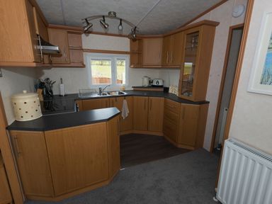 A kitchen with wooden cabinets a countertop a stove sink and window at The Lodge in Rhosybol