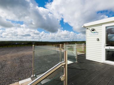 Exterior deck with glass railing and a gravel area with a rural landscape at The Lodge in Rhosybol