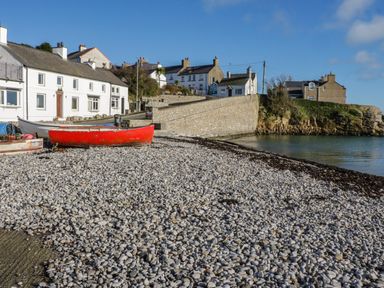 A pebble beach with boats and white houses near a stone wall by the water at The Lodge in Rhosybol