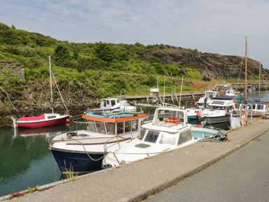 A harbor with multiple boats docked along a quay and rocky hills with greenery in the background at The Lodge in Rhosybol