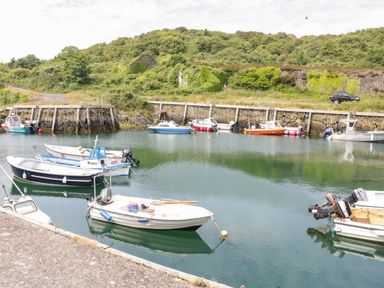 A small harbor with several boats moored in the water and a stone retaining wall with greenery in the background at The Lodge in Rhosybol