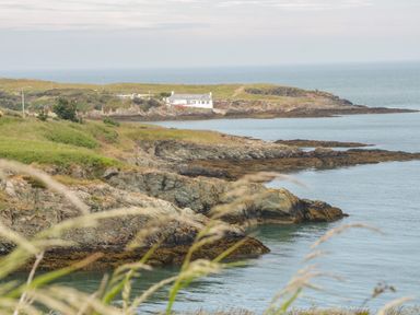 A coastal landscape with rocky cliffs and a white house near the water at The Lodge in Rhosybol