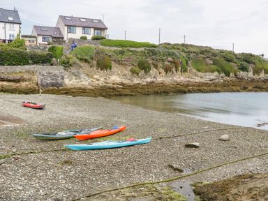 A rocky beach with kayaks and houses on a hill in the background at The Lodge in Rhosybol